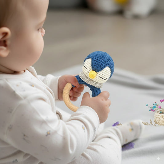 Baby holding a Knotty buds penguin rattle on a neutral background