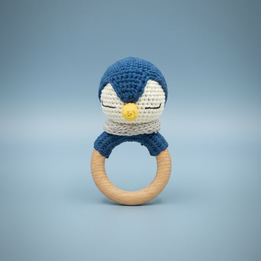 Crocheted penguin teething ring and rattle with blue and white design on a beige background