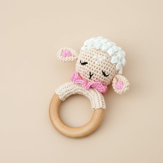 Crocheted sheep rattle with wooden ring on a beige background
